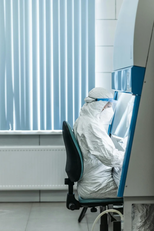 a man in a white suit sitting at a desk, by Rachel Reckitt, shutterstock, private press, staff wearing hazmat suits, door to lab, uk, profile image