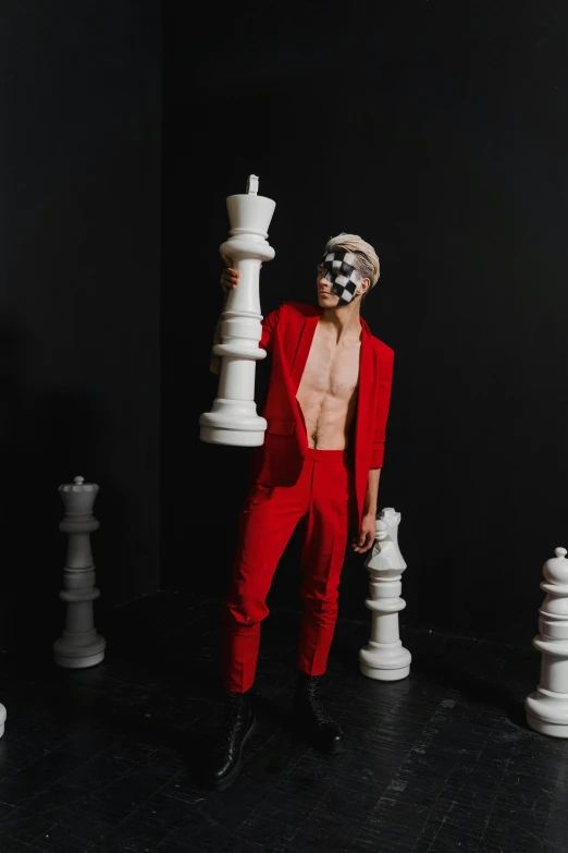 a man in a red suit standing in front of chess pieces, an album cover, inspired by Russell Dongjun Lu, pexels contest winner, maximalism, non binary model, bodypaint, jester, cai xukun
