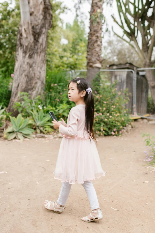 a little girl walking down a dirt road, inspired by Li Di, unsplash, prima ballerina in rose garden, holding a very advance phone, standing, lulu chen