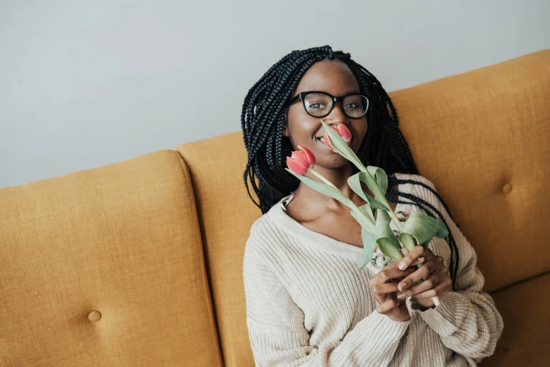 a woman sitting on a couch holding a bouquet of tulips, pexels contest winner, nerdy black girl super hero, flirting, girl with glasses, woman with braided brown hair