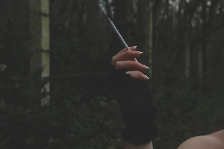 a close up of a person holding a cigarette, inspired by Elsa Bleda, unsplash, aestheticism, witch in the woods, ☁🌪🌙👩🏾, long boney limbs, grey skies