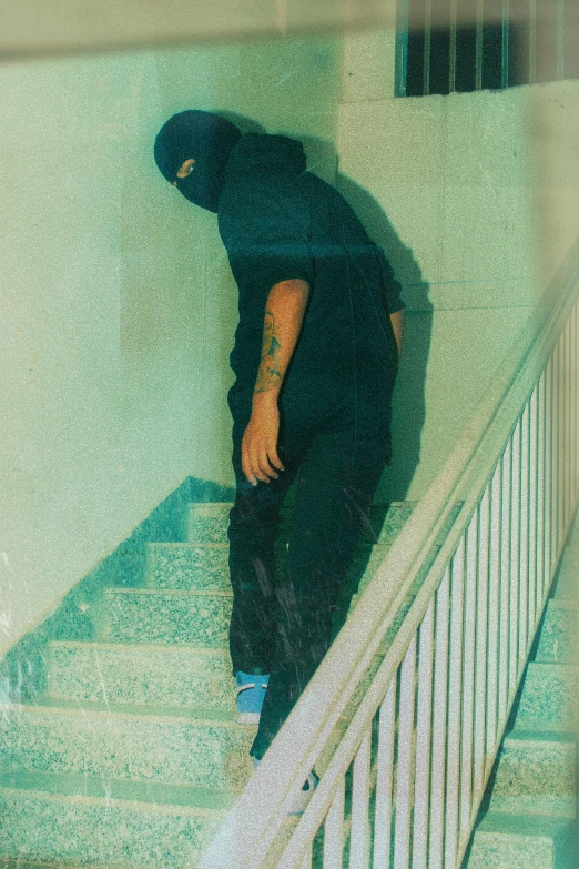 a person standing on a set of stairs, an album cover, unsplash, realism, balaclava covering face, low quality grainy, crime photos, teal aesthetic