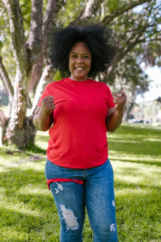 a woman standing on top of a lush green field, wearing pants and a t-shirt, red t-shirt, plus-sized, smiling