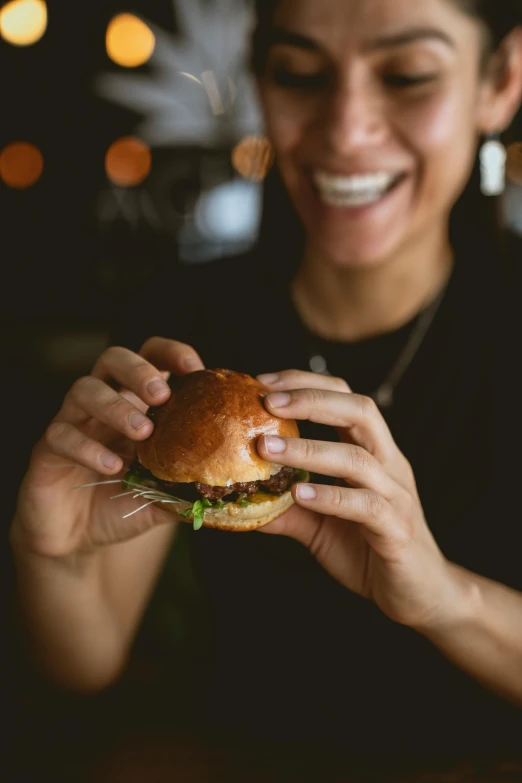 a woman holding a hamburger in front of her face, pexels, smiling for the camera, serving suggestion, low-key, organic detail