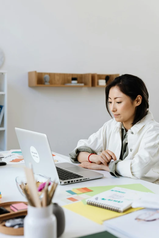 a woman sitting at a desk working on a laptop, trending on pexels, analytical art, with a lab coat, ethnicity : japanese, curated collections, idealised