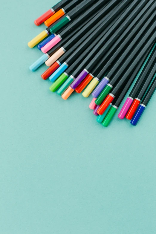 a bunch of pens sitting on top of a blue surface, colourful pastel, black and teal paper, zoomed in, detailed product shot