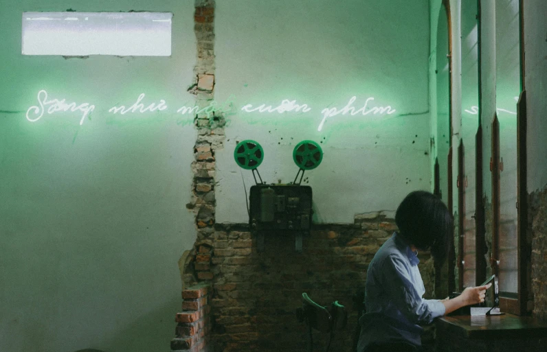 a woman sitting at a table in front of a neon sign, pexels contest winner, aestheticism, green alleys, white wall coloured workshop, wondering about others, studying in a brightly lit room