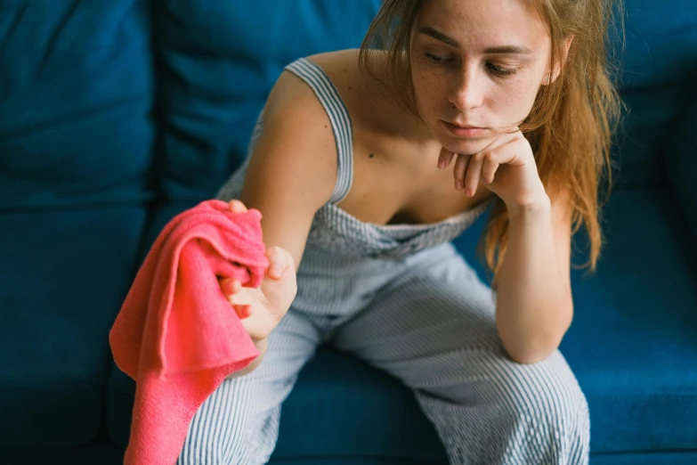 a woman sitting on a blue couch holding a pink towel, pexels, worn out clothes, dust and scratches, wearing an orange t-shirt, heartbreak