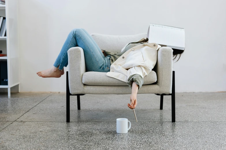 a woman sitting in a chair with a laptop on her lap, inspired by Sarah Lucas, trending on pexels, postminimalism, portrait of a woman sleeping, hat covering eyes, spilt coffee, minimalist furniture