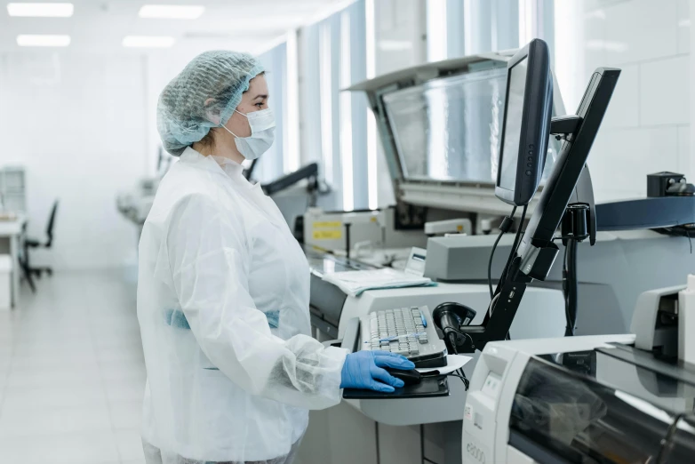 a woman in a lab coat working on a computer, a picture, shutterstock, stood in a factory, high-quality photo, surgical supplies, processor