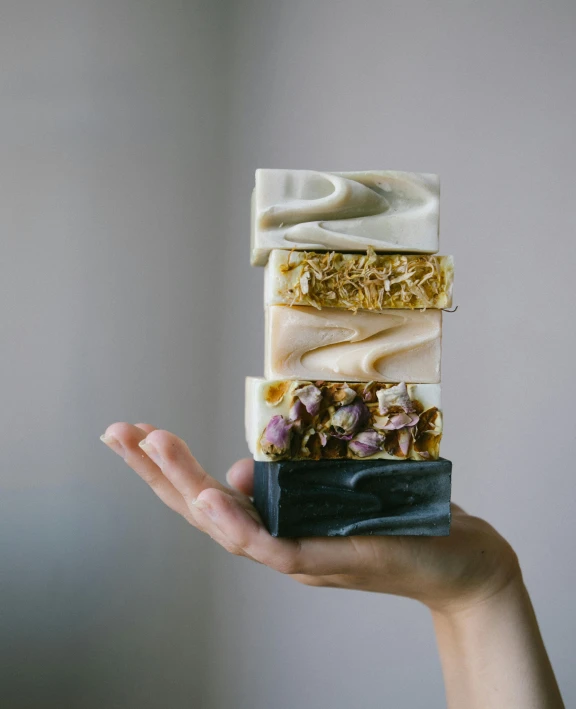 a person holding a stack of soap bars, by Alice Mason, unsplash, ivory and black marble, square, seeds, cake