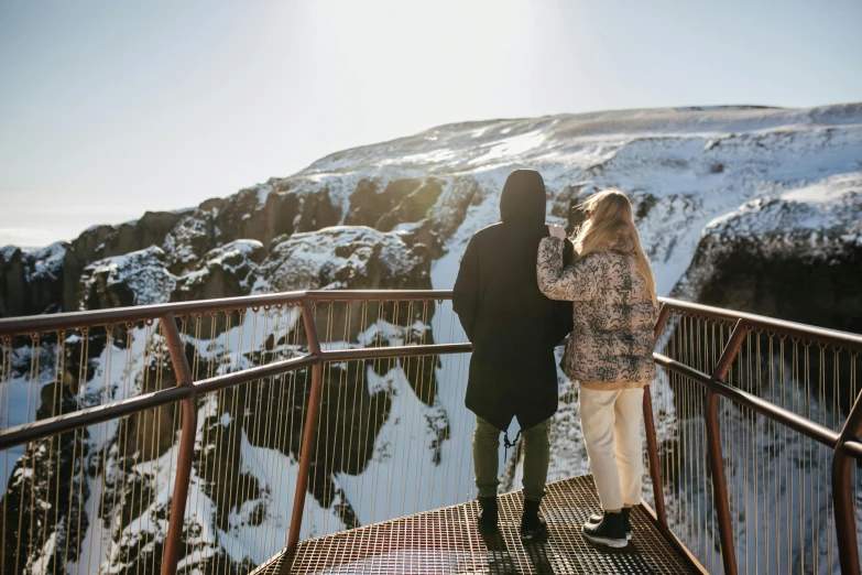 a couple standing next to each other on a bridge, by Hallsteinn Sigurðsson, trending on pexels, hurufiyya, snowy craggy sharp mountains, looking down a cliff, balcony, sunny day time