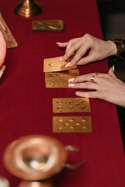 a close up of a person playing cards on a table, by Julia Pishtar, trending on pexels, art nouveau, golden orbs, brass sheet, brown, long
