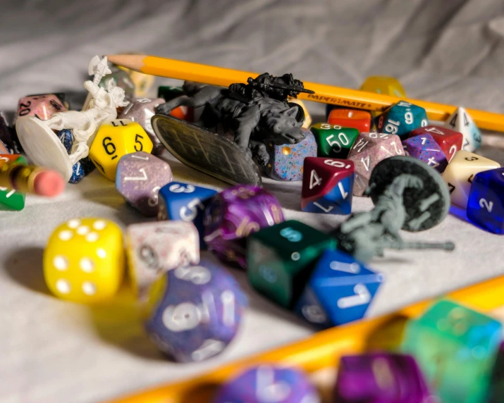 a pile of dice sitting on top of a table next to a pencil, hyperrealism, dungeons and dragons characters, multicoloured, toys, scrolls