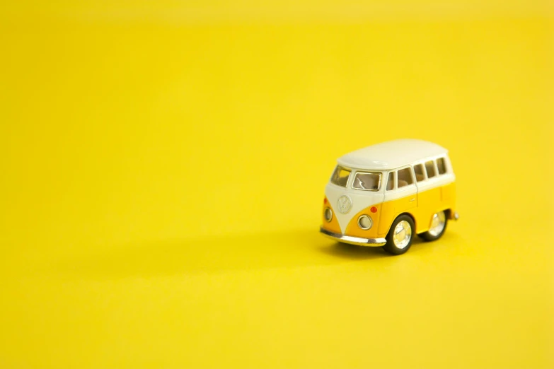 a yellow and white toy bus on a yellow surface, unsplash, fan favorite, beetle, miniatures