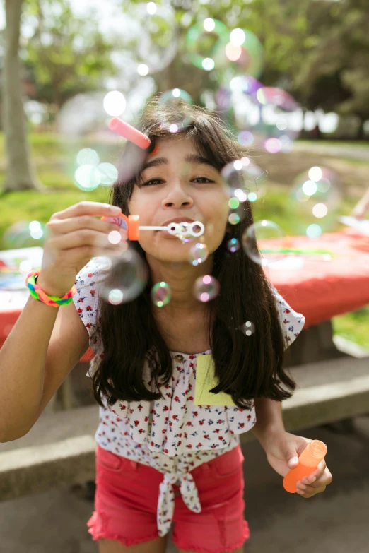 a young girl blowing bubbles in a park, by Michael Goldberg, promotional image, alanis guillen, more, - 9