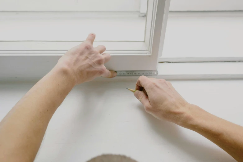 a person measuring the height of a window, inspired by Agnes Martin, pexels contest winner, square lines, plain background, hammershøi, low quality photo