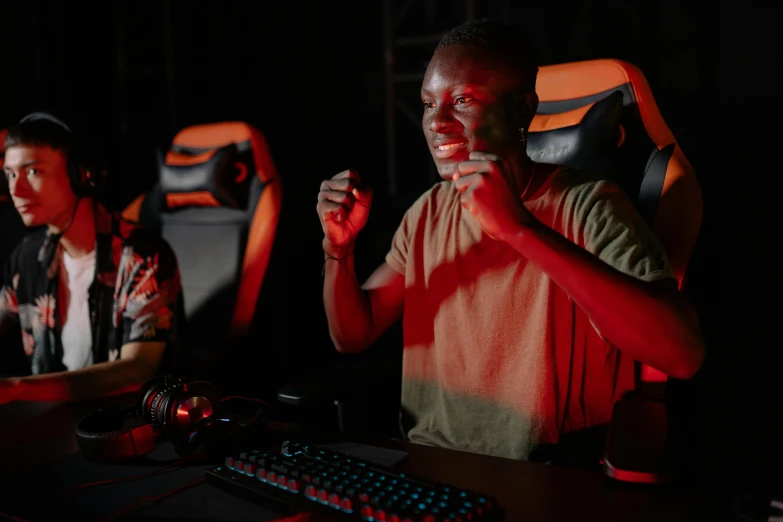 a couple of men sitting in front of a computer, pexels, realism, led gaming, red and orange colored, ( ( dark skin ) ), gaming chair