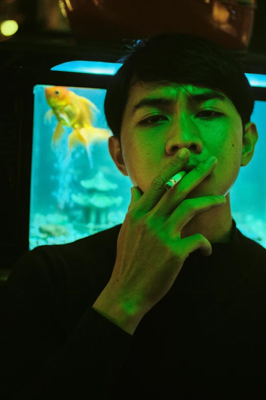 a man smoking a cigarette in front of a fish tank, an album cover, inspired by Liam Wong, pexels contest winner, realism, green lights, lips on cigarette, low quality photo, asian male