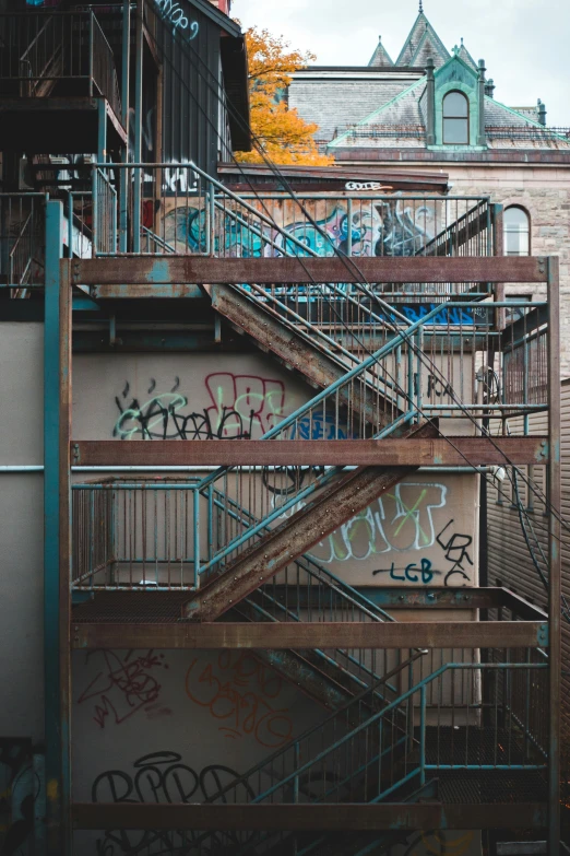 a fire escape staircase with a clock tower in the background, graffiti art, inspired by Elsa Bleda, pexels contest winner, graffiti, ((rust)), stairs to an upper floor, graffiti letters, dirty apartment