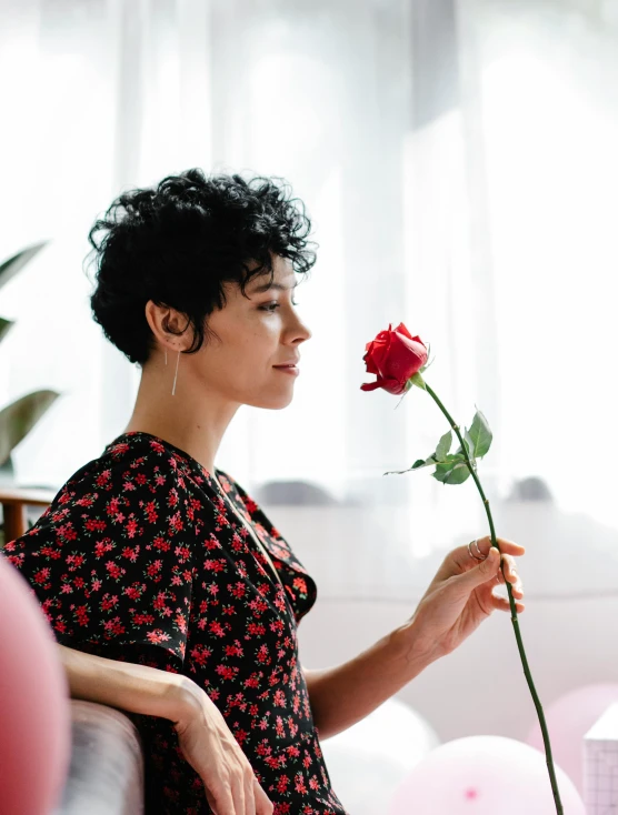 a woman sitting on a couch holding a flower, trending on pexels, curly pixie cut hair, growing out of a giant rose, profile image, androgynous male