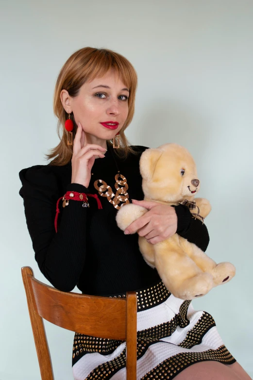 a woman sitting on a chair holding a teddy bear, inspired by Leila Faithfull, trending on reddit, gold and red accents, 1960s-era, jewelry, dasha taran