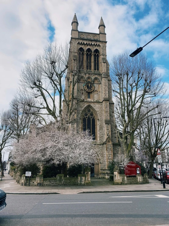 a car driving down a street next to a tall building, an album cover, inspired by Richmond Barthé, pexels contest winner, at highgate cemetery, cherry blossom tree, exterior view, church