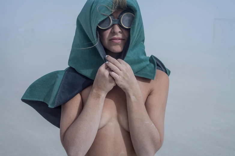 a woman standing on top of a sandy beach, an album cover, inspired by Ren Hang, unsplash contest winner, wearing victorian goggles, dark green cloak, shirtless, burka