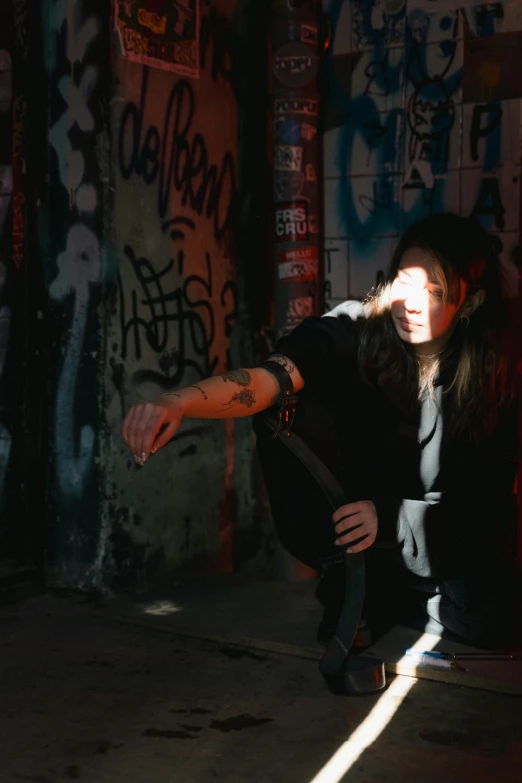 a woman sitting on the ground in front of a graffiti covered wall, light behind, threatening pose, 2019 trending photo, concert photo