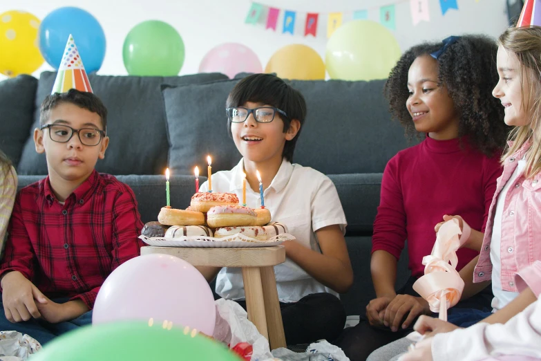 a group of children sitting around a table with a birthday cake, 15081959 21121991 01012000 4k, full body image, riyahd cassiem, balloons