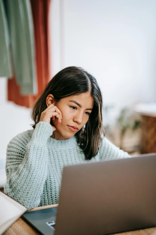 a woman sitting in front of a laptop computer, trending on pexels, wearing a green sweater, asian descent, hovering indecision, grey