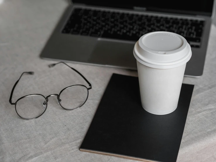 a laptop computer sitting on top of a table next to a cup of coffee, by Carey Morris, trending on pexels, postminimalism, in square-rimmed glasses, paper cup, on a gray background, no - text no - logo