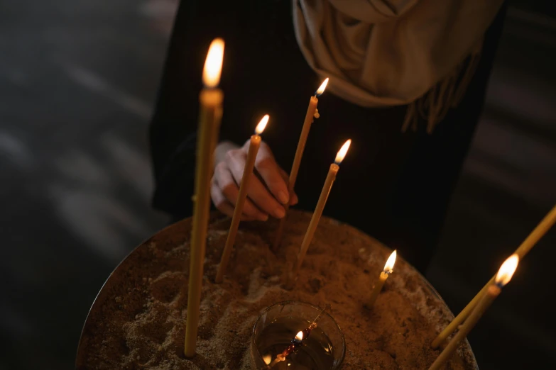 a close up of a person lighting candles on a cake, by Julia Pishtar, orthodox, fan favorite, standing inside of a church, brown