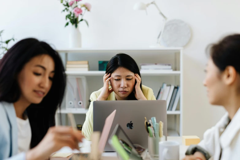 three women sitting at a table in front of a laptop, by Julia Pishtar, trending on pexels, people panic in the foreground, an asian woman, sitting behind desk, ad image