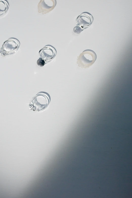 a bunch of rings sitting on top of a table, by Nina Hamnett, minimalism, water particulate, clear detail, overhead sun, hanging