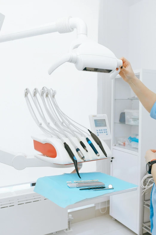 a woman sitting in a chair in a dentist's office, by Adam Marczyński, shutterstock, extended robotic arms, holding a crowbar, detailed product image, with a whitish