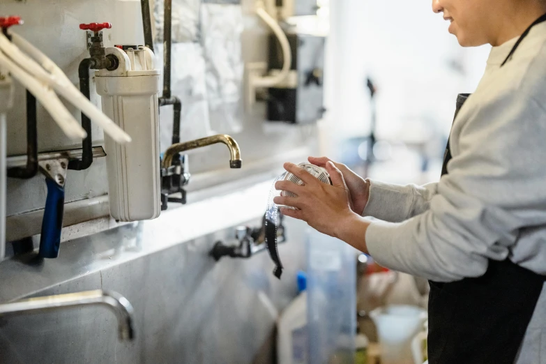 a woman washing her hands in a kitchen, by Daniel Lieske, pexels, wearing plumber uniform, holding a drink, at the counter, profile image