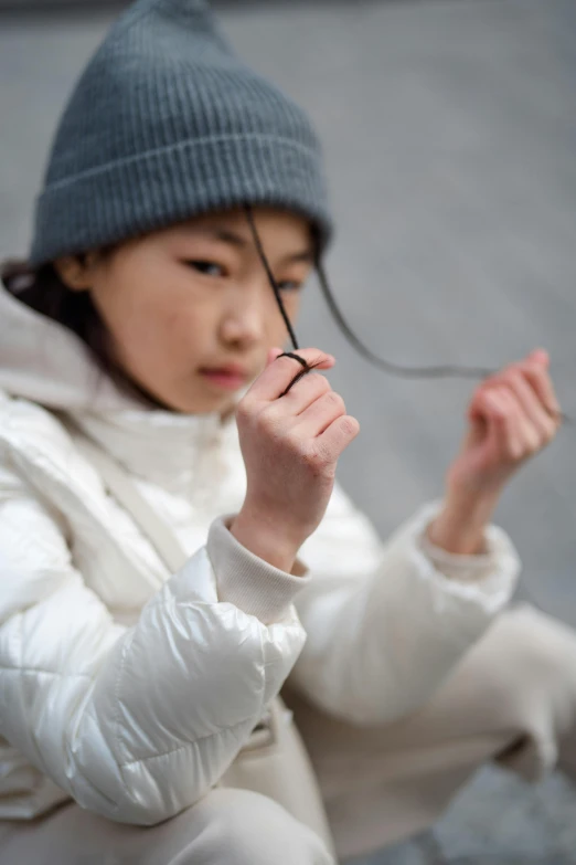 a little girl sitting on a bench with a cell phone in her hand, an album cover, inspired by Kanō Naizen, unsplash, thin wires, beanie, yin zhen chu, dynamic closeup