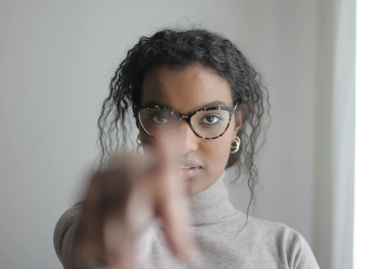 a woman in glasses pointing at the camera, pexels, hurufiyya, ( ( dark skin ) ), mixed race, square rimmed glasses, threatening pose