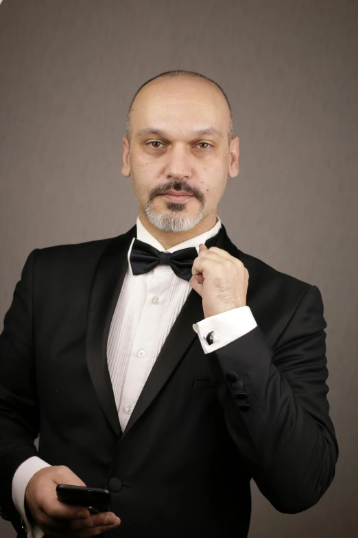 a man in a tuxedo holding a cell phone, an album cover, inspired by Cristache Gheorghiu, pixabay, portrait of bald, striking a pose, studio portrait photo, arab man