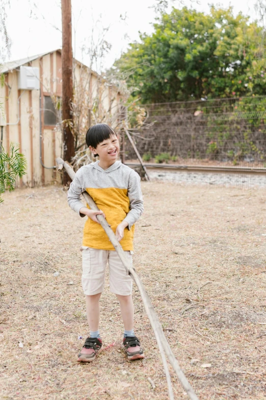 a little boy that is standing in the dirt, inspired by Matsumura Goshun, unsplash, shin hanga, holding a yellow toothbrush, in the yard, wearing farm clothes, holding a giant flail