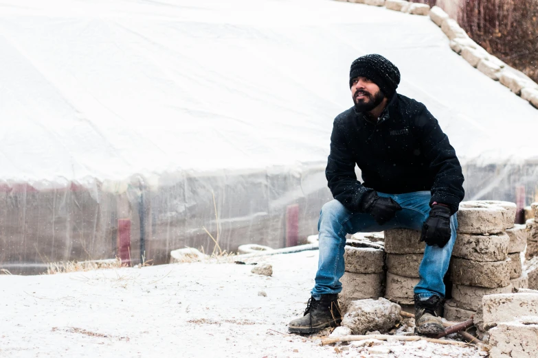 a man sitting on top of a pile of rocks, he also wears a grey beanie, matt berry, in the winter, real life photo of a syrian man