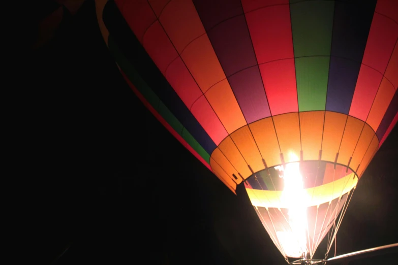 a hot air balloon is lit up at night, happening, miranda meeks, view from the ground, lit from the side, coloured