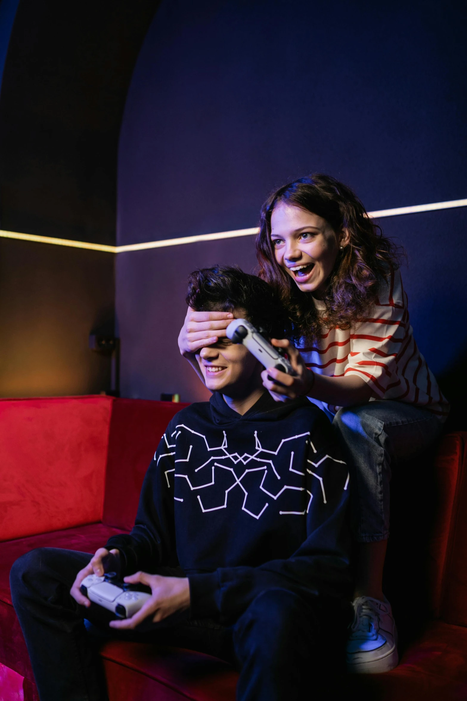 a man and a woman sitting on a red couch playing a video game, by Julia Pishtar, interactive art, curls on top of his head, taking control while smiling, studio lit, teenage boy