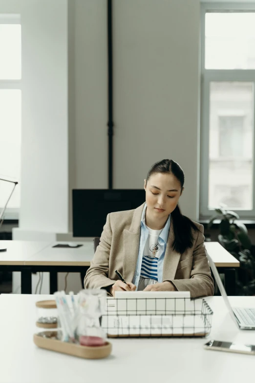 a woman sitting at a desk working on a laptop, inspired by Fei Danxu, pexels contest winner, architect studio, writing on a clipboard, standing in class, gif