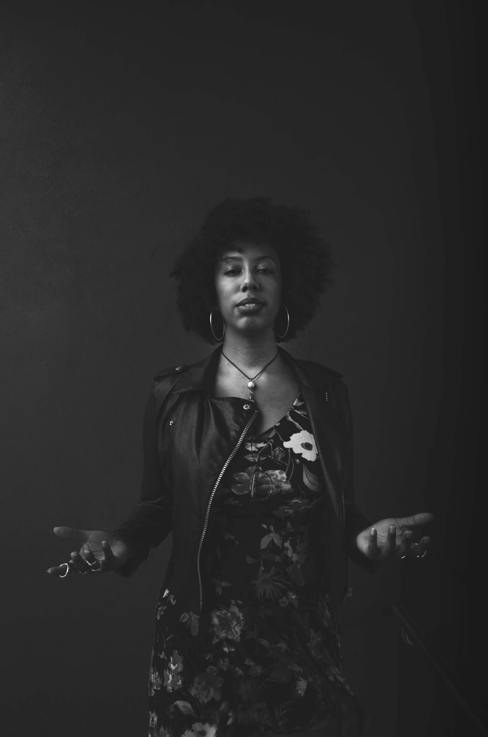 a woman in a black and white photo, a black and white photo, inspired by Carrie Mae Weems, unsplash, she wears leather jacket, stands in center with open arms, afro, flower child