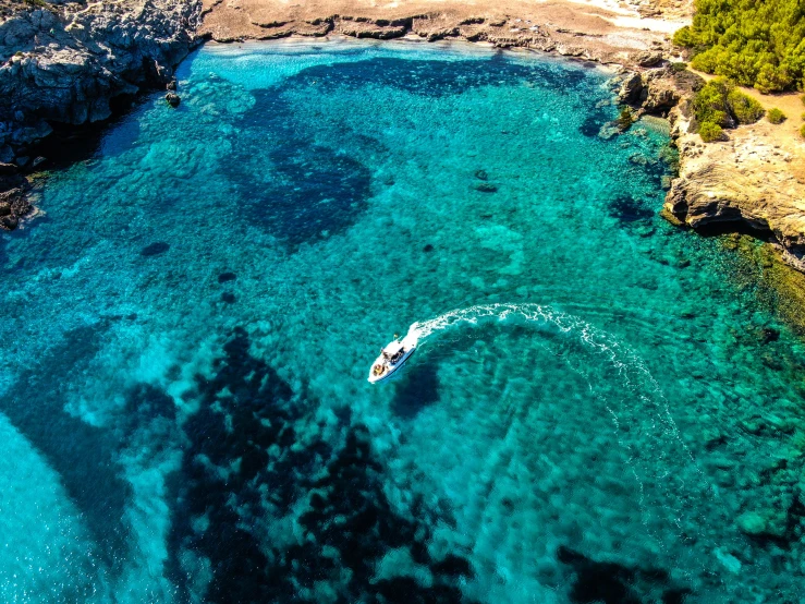 a boat that is in the water near some rocks, by Simon Marmion, pexels contest winner, wide aerial shot, crystal clear blue water, apulia, slide show