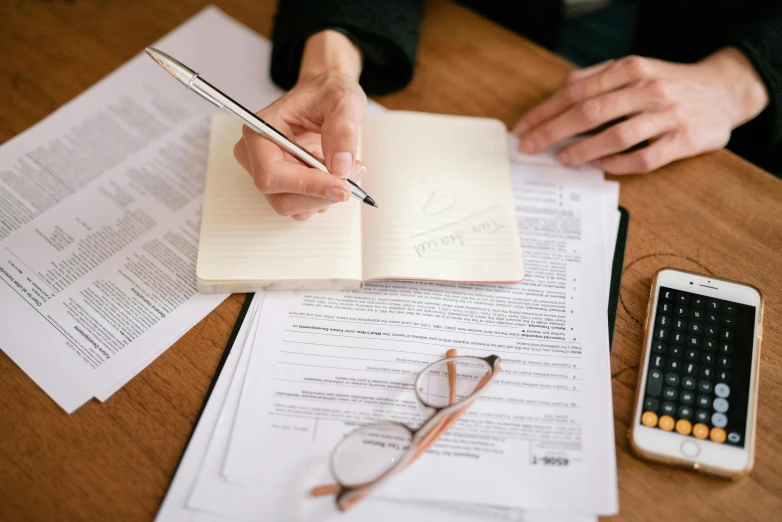 a person sitting at a table with papers and a calculator, instagram picture, professional grade, thumbnail