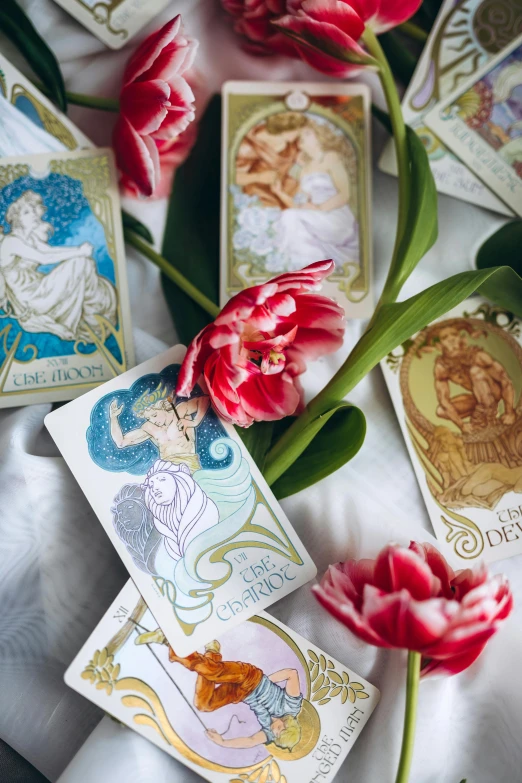 a bunch of cards sitting on top of a table, inspired by Alphonse Mucha, trending on pexels, art nouveau, bed of flowers on floor, astrology, goddess of spring, white