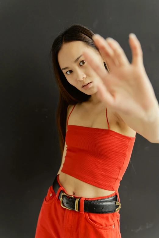 a woman in a red top is making a stop sign, an album cover, inspired by Feng Zhu, trending on pexels, bare midriff, at a fashion shoot, gestures, wearing a camisole